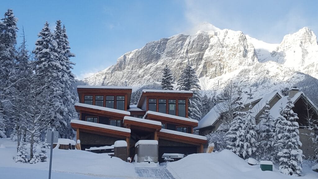Custom luxury mountain home exterior with wood trim and large windows in winter