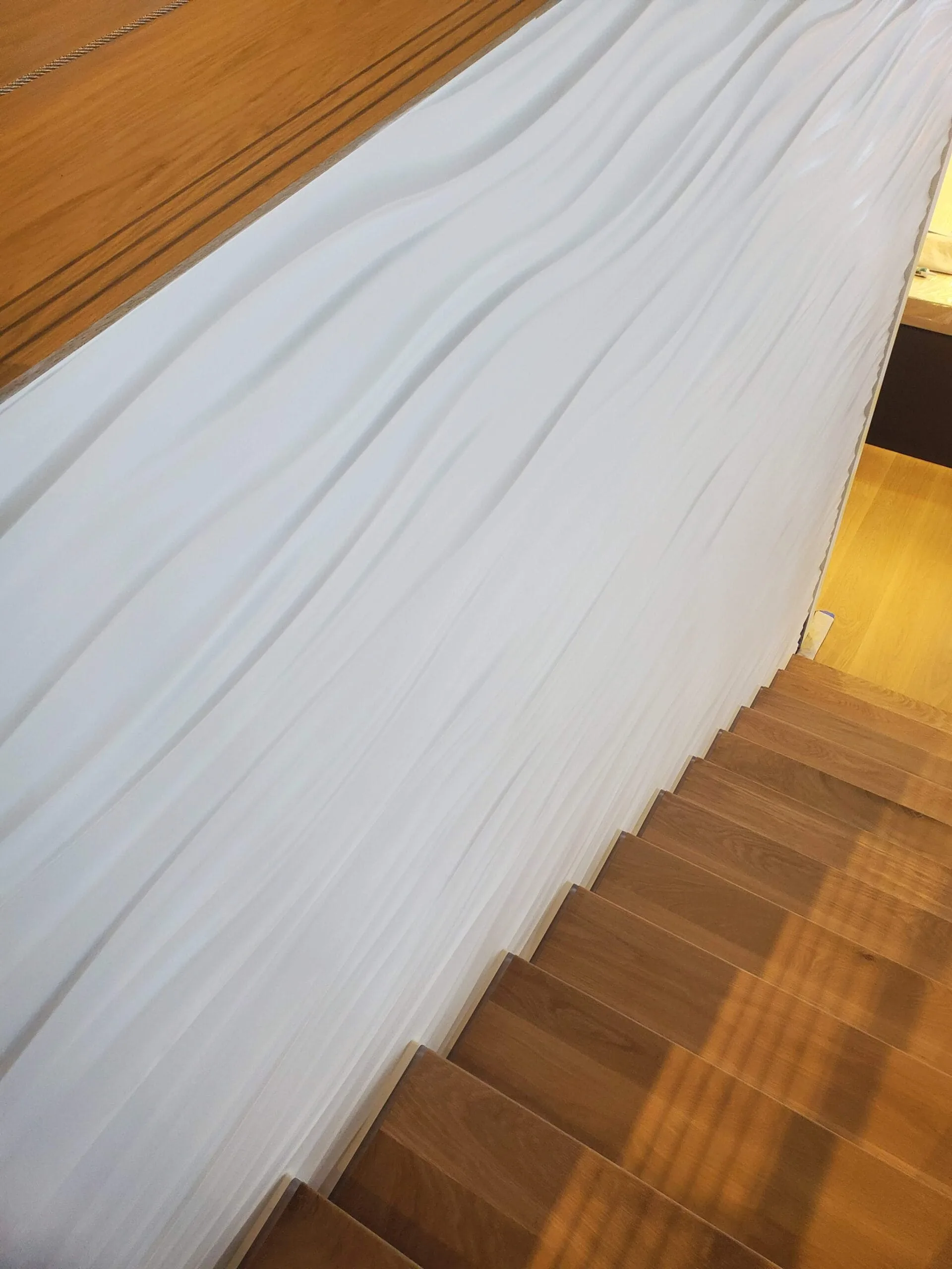 Hardwood stair treads descending beside a wave-textured feature wall