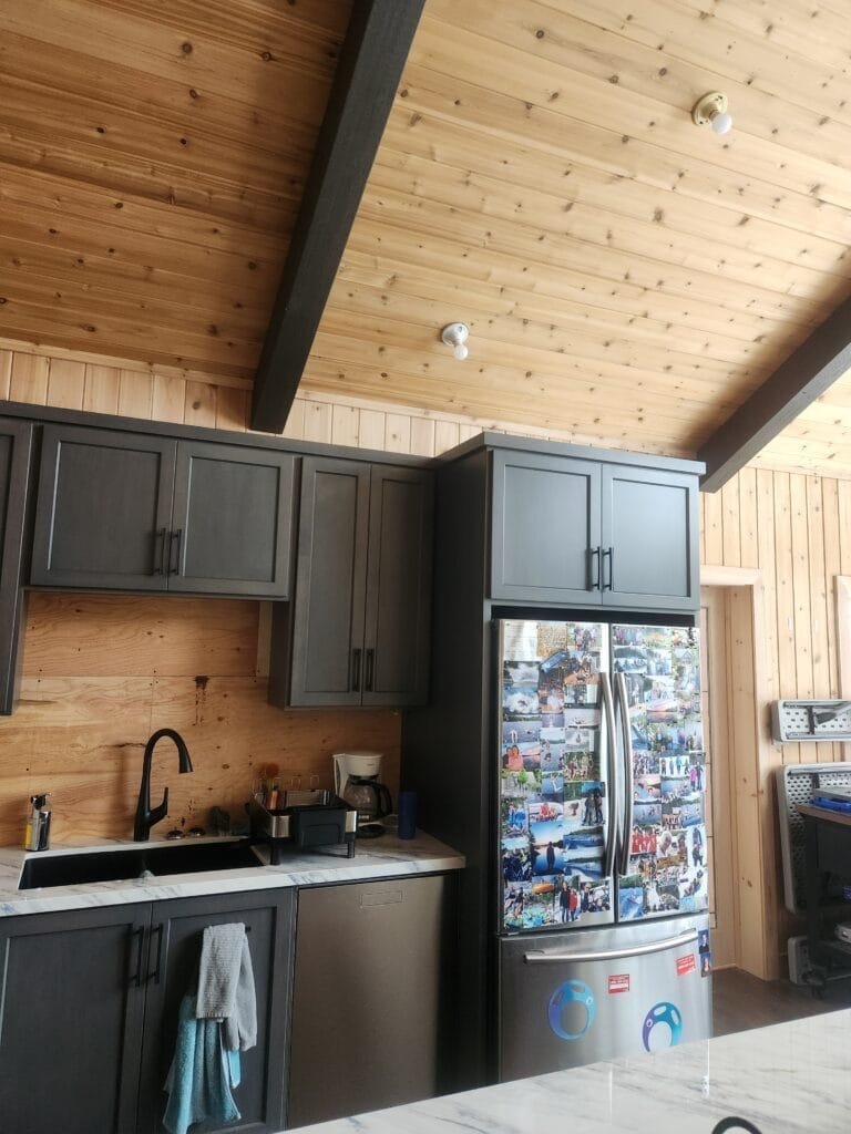 Custom grey kitchen cabinetry with pine tongue-and-groove ceiling and dark beams